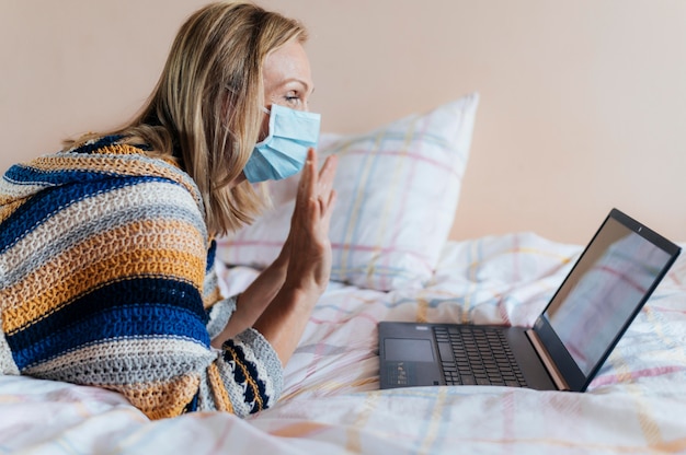 Woman with medical mask in quarantine at home with laptop