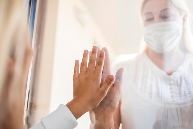 Woman with medical mask in quarantine behind window with child