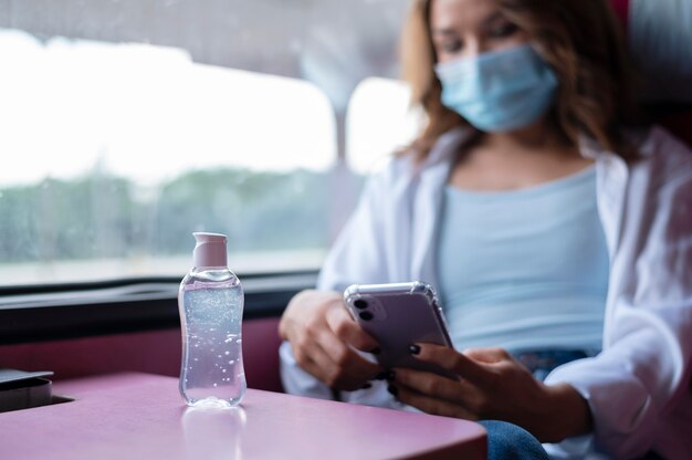 Woman with medical mask traveling by public train and using smartphone