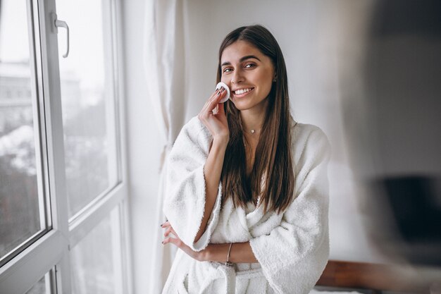 Woman with mirror removing makeup with pad