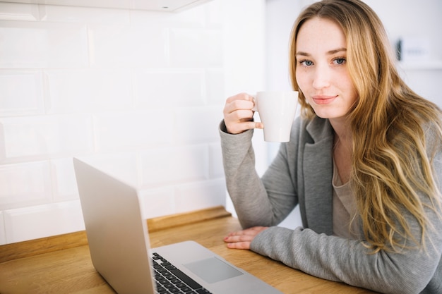 Free photo woman with mug and laptop in kitchen