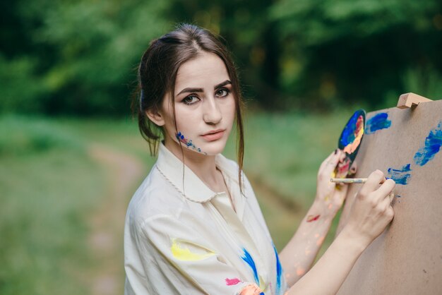 Woman with painted colorful face drawing on a canvas