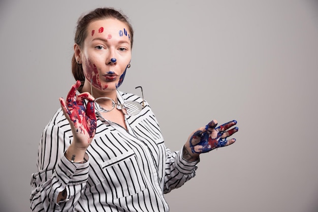 Woman with paints on her face puts on glasses on gray