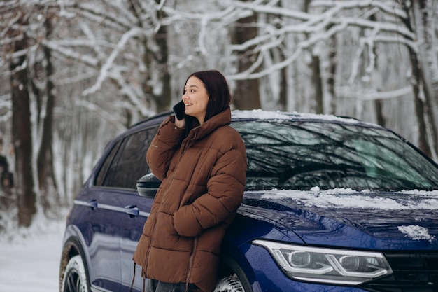 Woman with phone standing by her car in winter forest