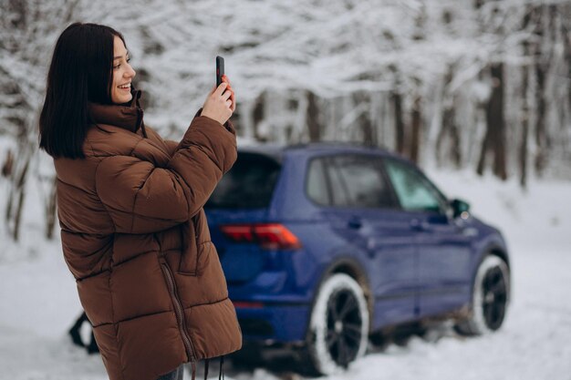 Woman with phone standing by her car in winter forest