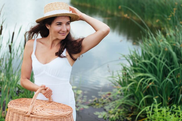 Woman with picnic basket posing by the lake