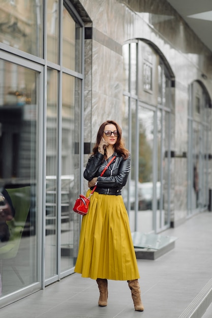 Woman with red handbag walking while speaking on the phone near a business building