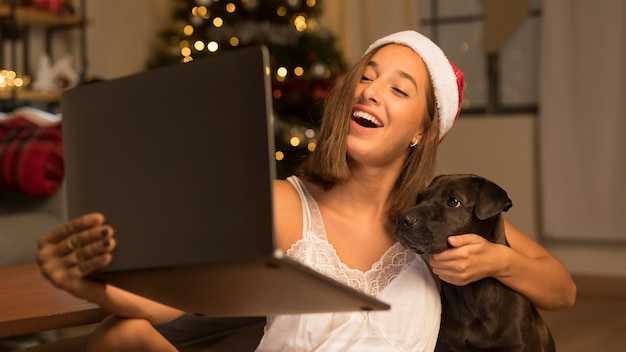 Free photo woman with santa hat showing her dog to people on call using laptop