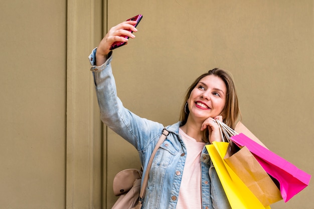 Free photo woman with shopping bags taking selfie at wall