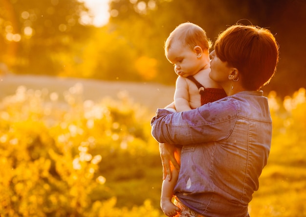 Free Photo woman with short hair kisses her child standing on lawn in the evening 