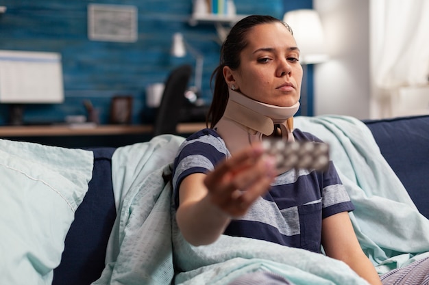 Free Photo woman with sickness and cervical foam collar on couch taking medical treatment for back and neck pain. caucasian adult with muscular contracture after physical injury in accident