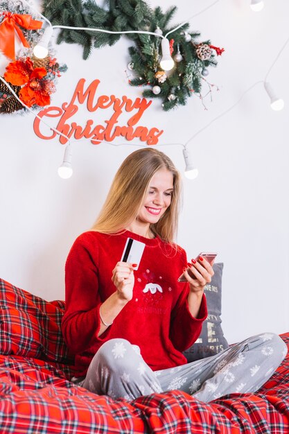 Woman with smartphone and plastic card on bed