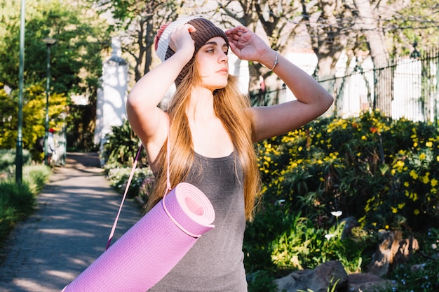 Woman with stretching mat adjusting hat