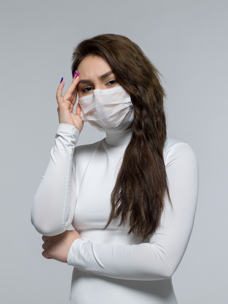 Woman with strong headache holding her temple in white sterile mask