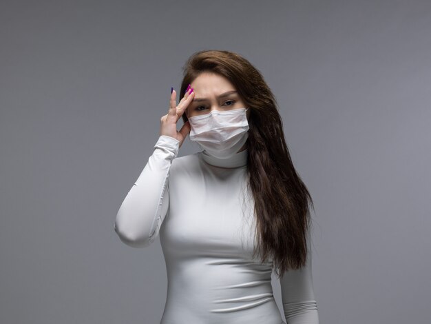 Woman with strong headache in white protective mask