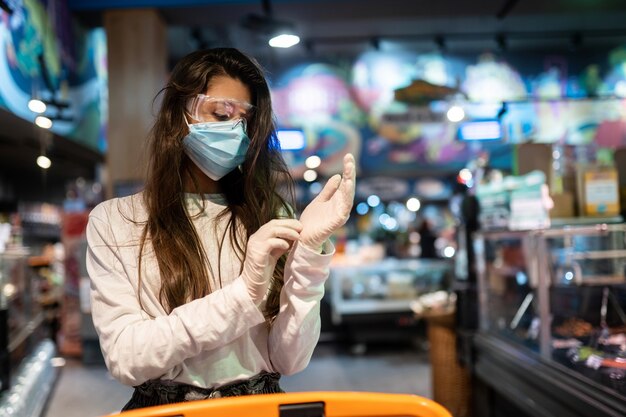 Woman with the surgical mask and the gloves is shopping in the supermarket