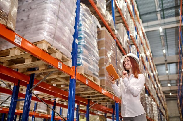 Woman with tablet working near warehouse shelves with cargo