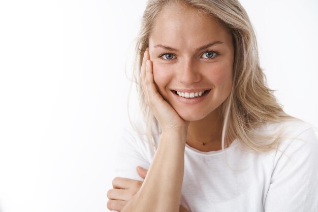 woman with tattoo leaning on arm and gazing with flirty sensual gaze at camera smiling lovely at camera expressing tenderness gentle feelings on white wall