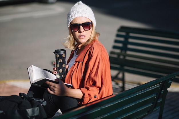 Woman with thermos reading on bench