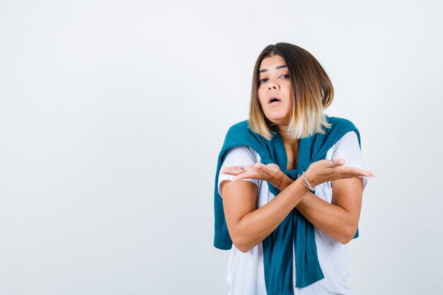 Woman with tied sweater in white t-shirt showing helpless gesture and looking confused , front view.