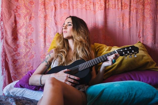 Woman with ukulele leaning on pillows