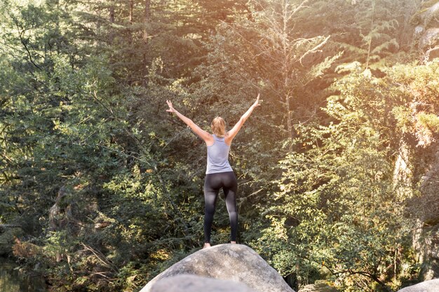 Woman with upped hands on stone near forest