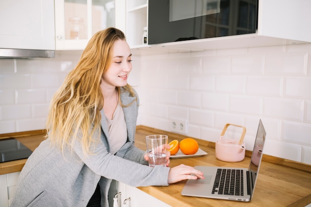 Free photo woman with water using laptop in kitchen