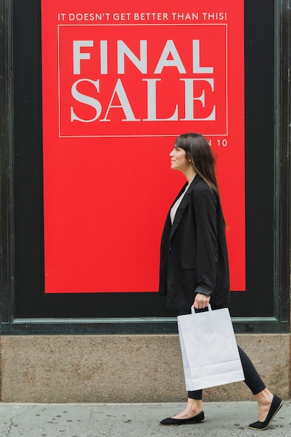 Free photo woman with white shopping bag walking near shop