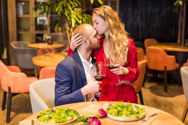 Free photo woman with wine glass kissing man on forehead