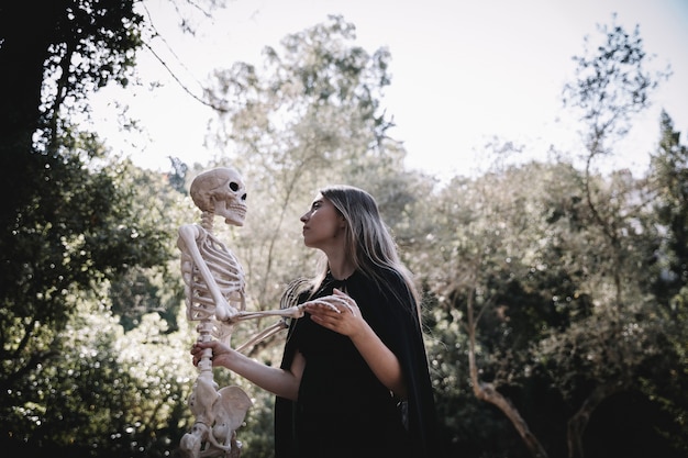 Free photo woman in wizard clothes looking attentive at skeleton