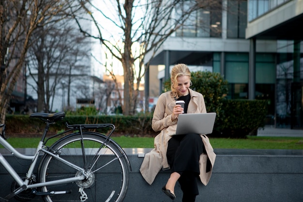 Free Photo woman working on her laptop outside and drinking coffee