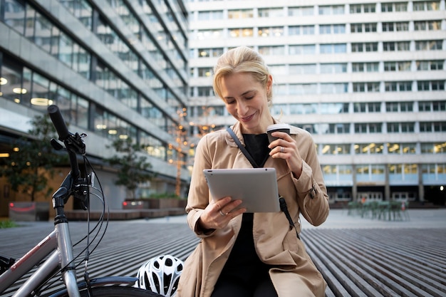 Free photo woman working on her tablet outside and drinking coffee