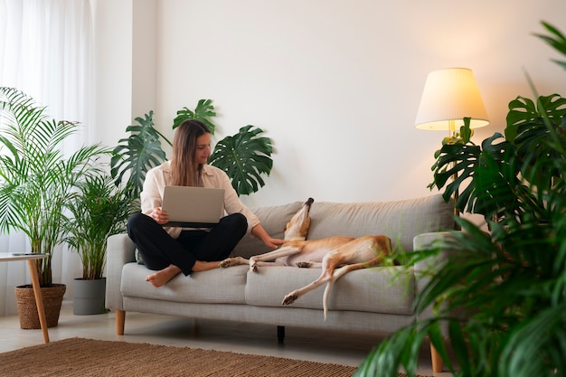 Free photo woman working at home from laptop with greyhound dog on the couch