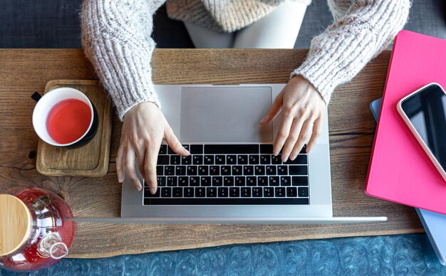 Woman working on a laptop in a cafe with a cup of tea top view