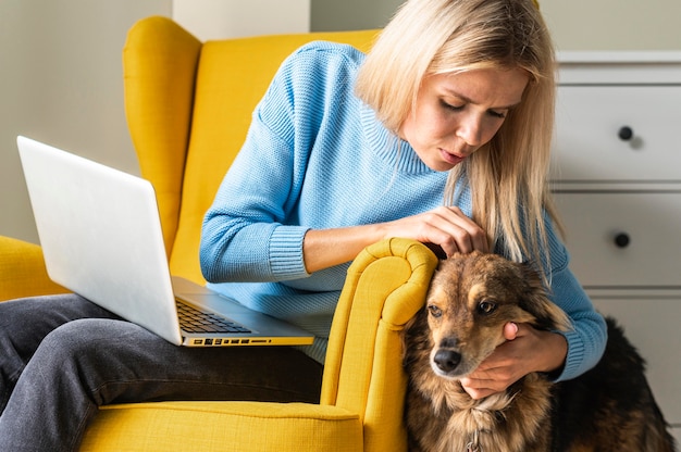 Free photo woman working on laptop from armchair during the pandemic and petting her dog