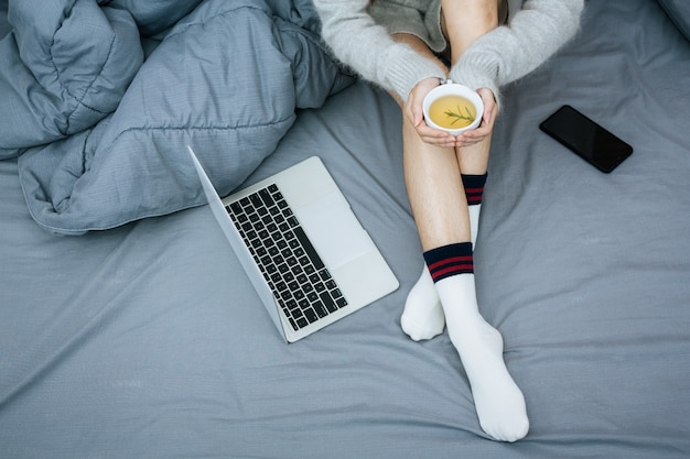 Woman working on laptop on her bed in cold day