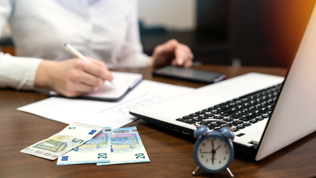 Free photo woman working with finances on the table. laptop, smartphone, money, notepad, clock