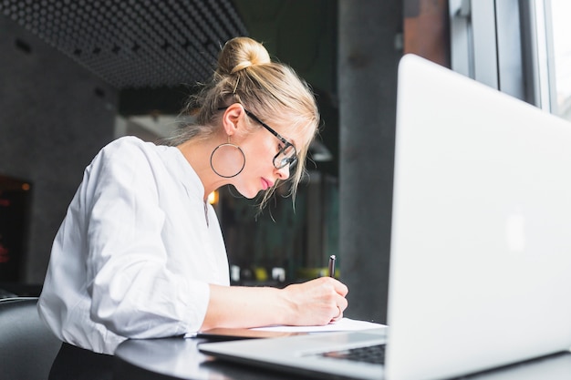 Free Photo woman writing on document with laptop on desk