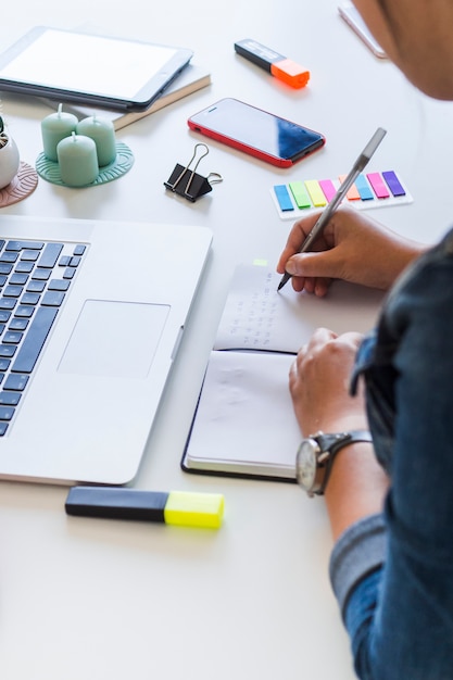 Woman writing in notebook on table with laptop and equipments