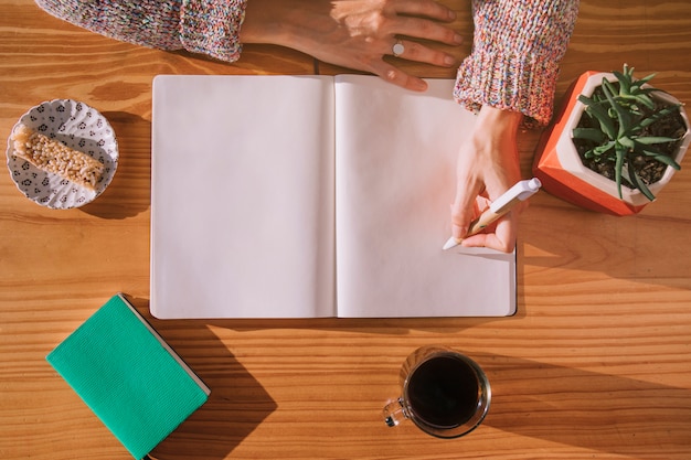 Woman writing on pen with blank white notebook over the wooden desk