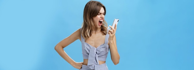 Free Photo woman yelling at smartphone with sick and tired look being agressive and angry swearing on boyfriend who dumbed her on phone holding hand on waist looking with hate at cellphone screen