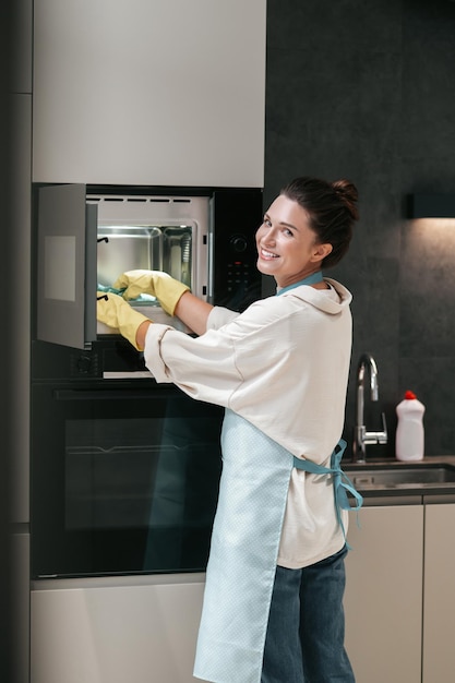 A woman in yellow gloves cleaning the oven