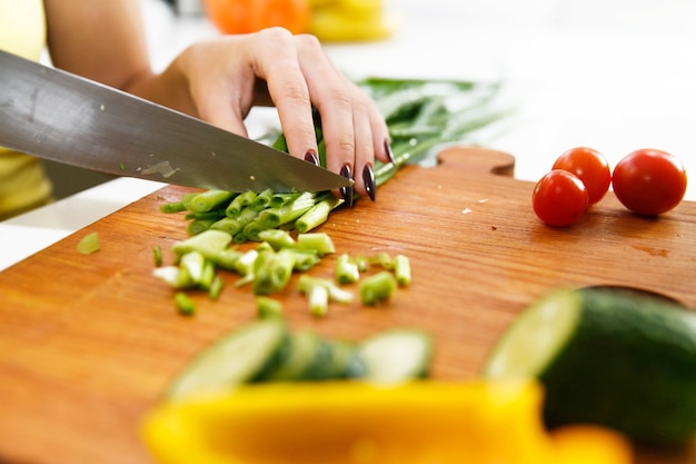 Free photo woman in yellow shirt cuts green onion in the kitchen