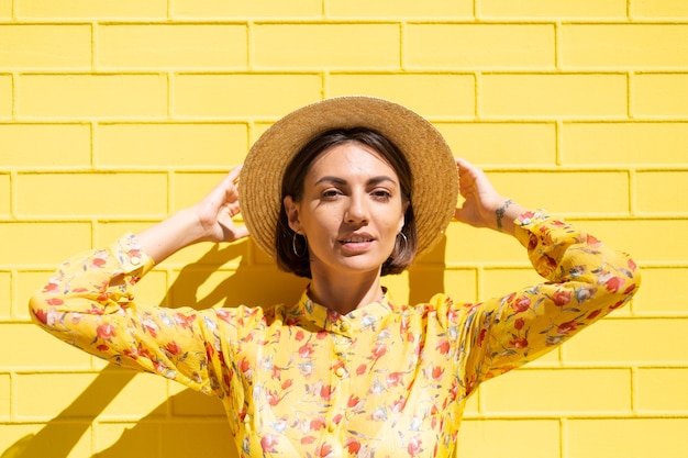 Free photo woman in yellow summer dress and hat on yellow brick wall calm and positive