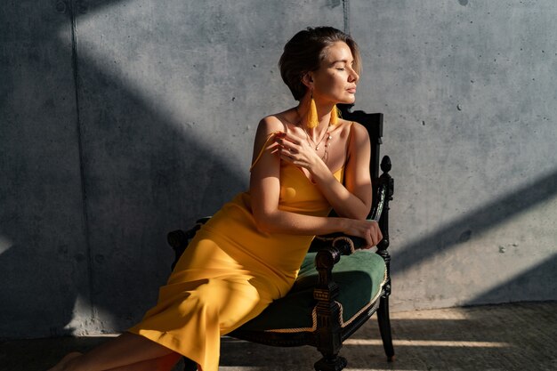 woman in yellow summer dress with short hairstyle in interior room concrete wall posing