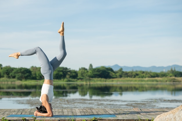 Free photo woman on a yoga mat to relax in the park. young sporty asian woman practicing yoga, doing headstand exercise, working out, wearing sportswear, pants and top.