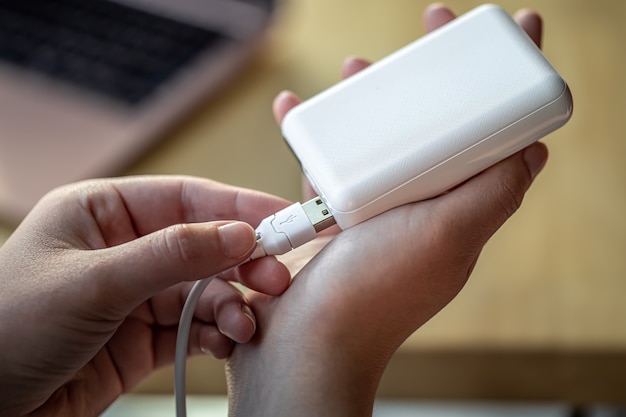 Womans hand holding white usb cable and white power bank