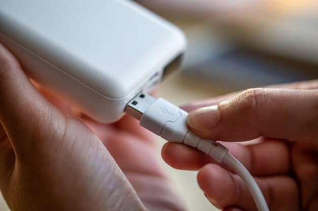 Womans hand holding white usb cable and white power bank