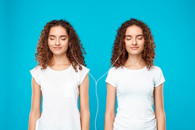 Free photo womans twins listening music in headphones, smiling over blue.