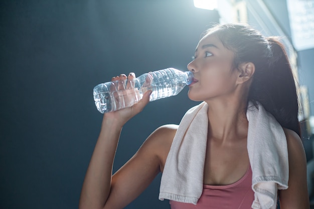 Women after exercise drink water from bottles and handkerchiefs in the gym.